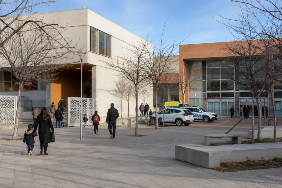 Ciudadanos acceden a una escuela pública y a un centro de salud en una plaza urbana española, reflejando el impacto de la financiación autonómica en los servicios públicos.