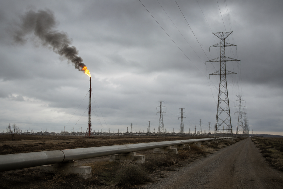 Infraestructura energética con un mechurrio de gas en funcionamiento y varias torres de alta tensión extendiéndose hacia el horizonte bajo un cielo gris, reflejando la presión sobre los costes energéticos en España.